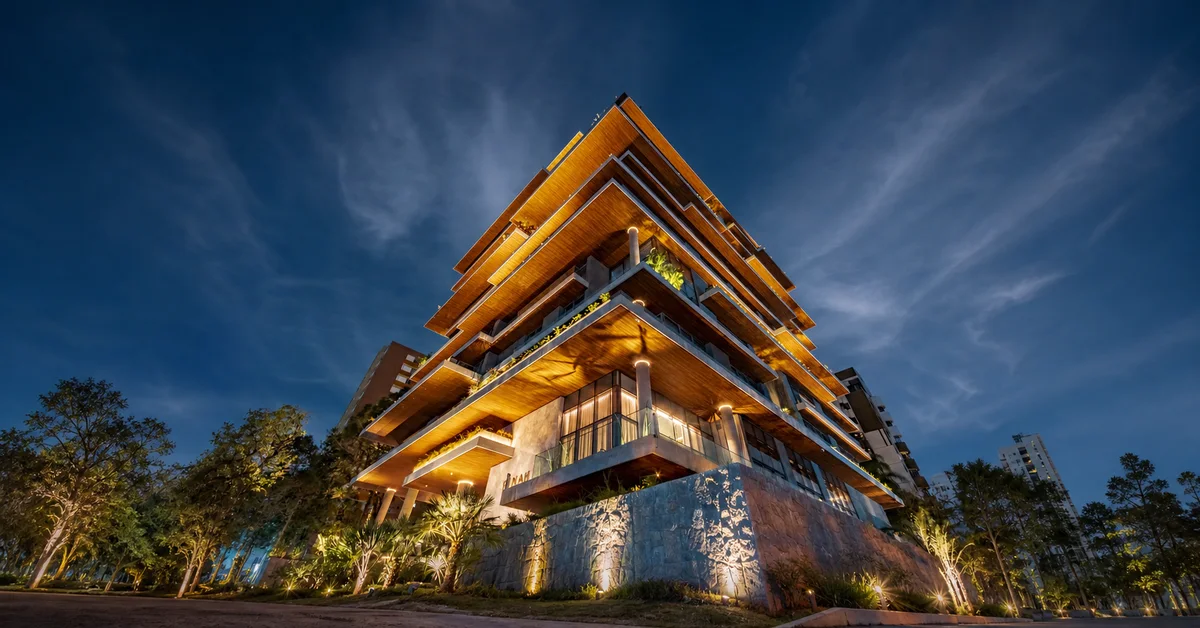 Fachada de edifício residencial contemporâneo em Curitiba, com madeira, pedra, iluminação arquitetônica e araucárias ao entardecer.